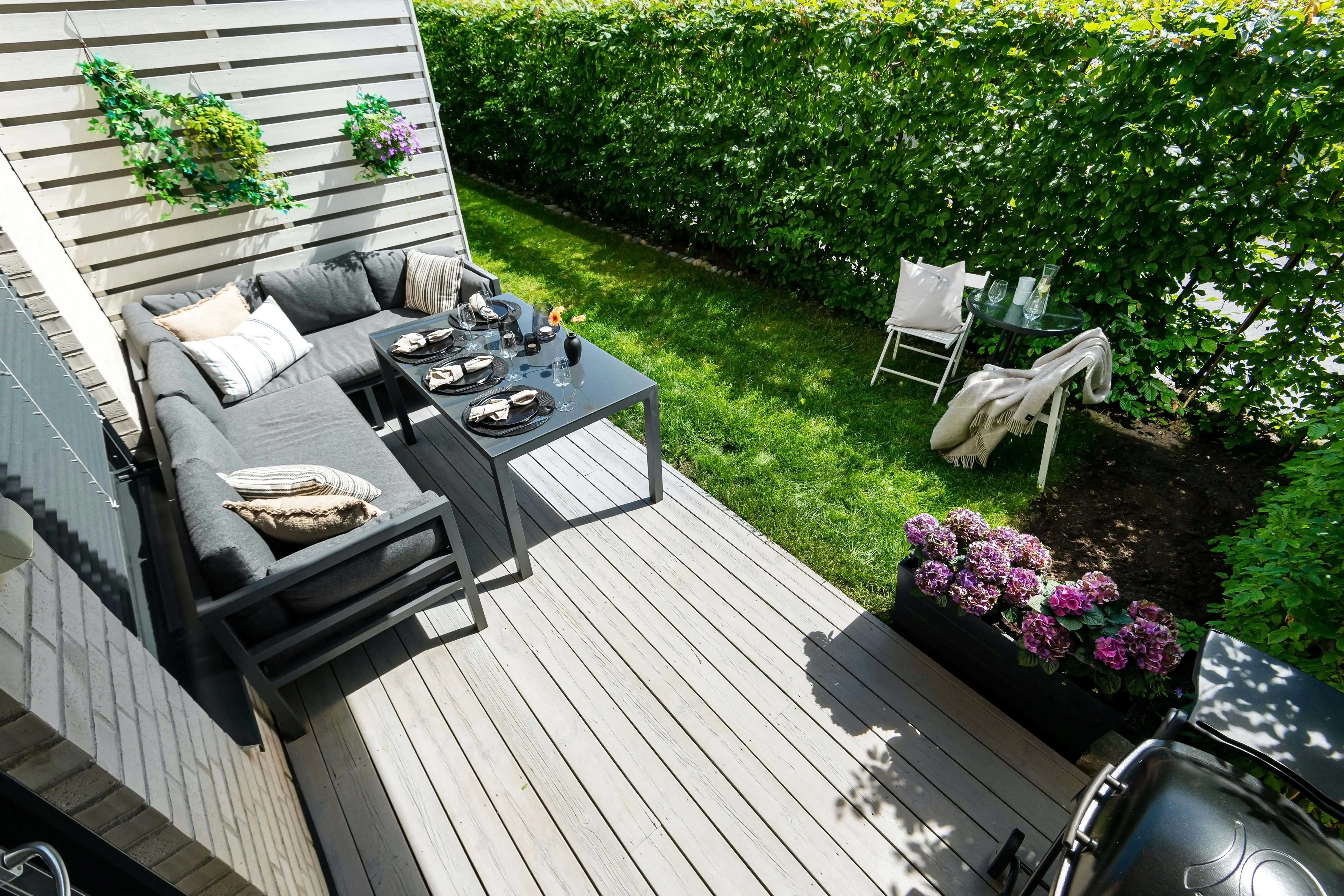 Stylish outdoor patio with furniture, greenery, and a grill, perfect for summer relaxation.